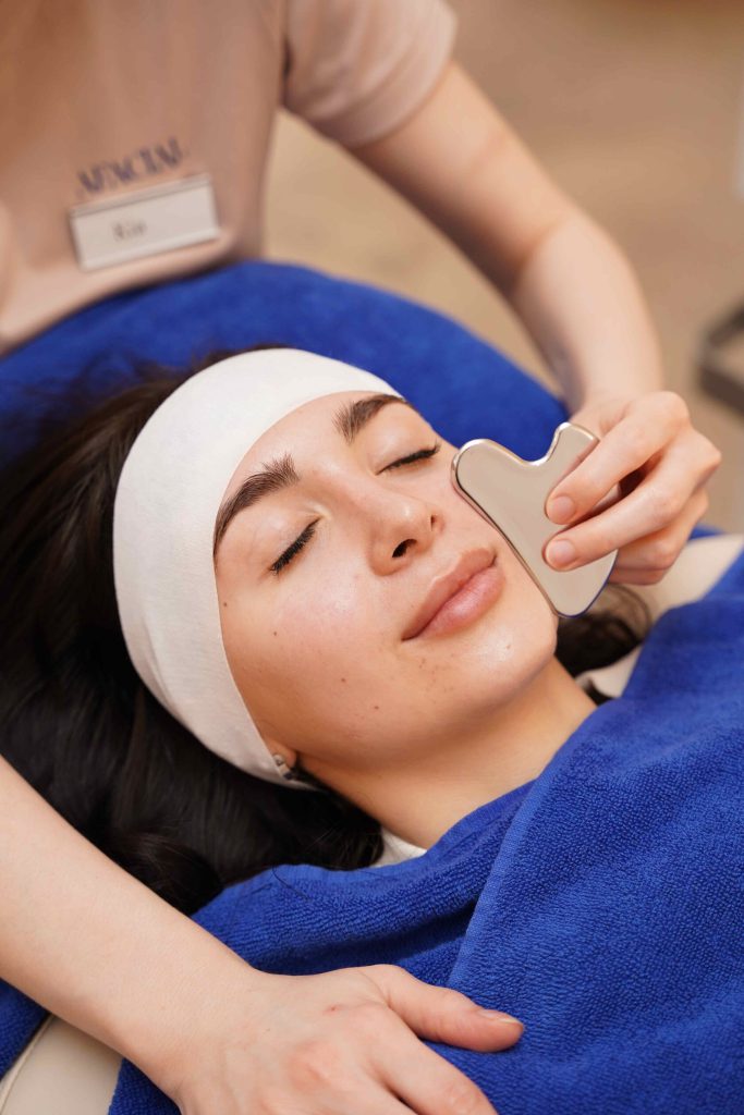 Gua-Sha-Stein am Gesicht der liegenden Kundin - Abschluss der Anti Aging Behandlung in Wien