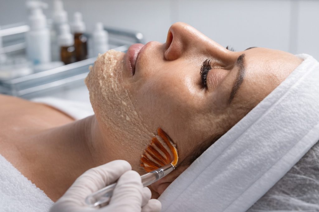Kosmetikerin trägt mit einem Pinsel eine Peeling-Maske zur porentiefen Gesichtsreinigung auf